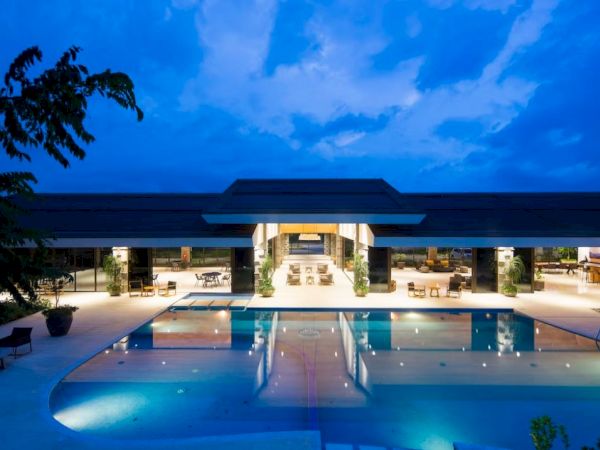 A modern hotel courtyard pool glows at dusk beneath a blue sky with patio seating under a sleek building canopy.