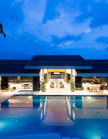 A modern resort with a lit outdoor swimming pool and lounge chairs under a vivid blue dusk sky.