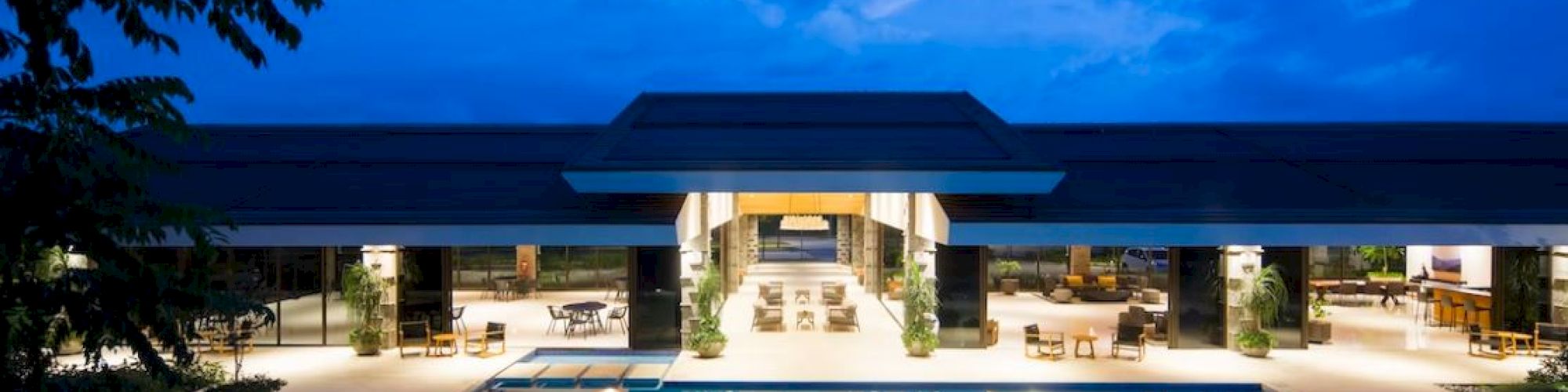 A modern hotel courtyard pool reflecting a blue twilight sky beneath palm trees and warm lights at dusk.