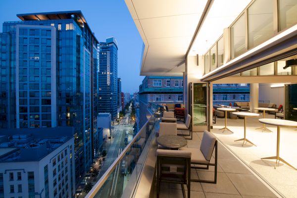 A modern high-rise rooftop terrace overlooks a city skyline of glass buildings and streetlights below.