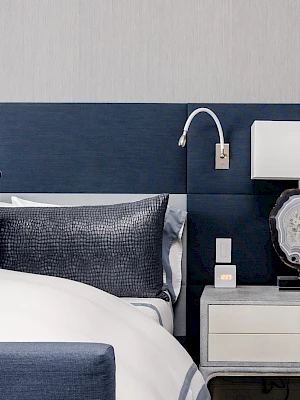A modern bedroom with a bed, blue pillows, a bedside table, wall sconce/phone charger, and a decorative geode lamp.