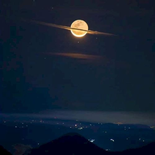 A bright full moon and a glowing meteor-like streak hover over dark mountains and a night sea of lights.