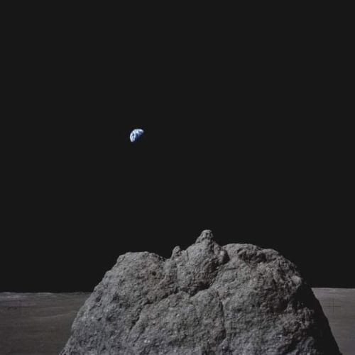 A tiny blue planet/moon floats above a gray rock against a dark, nearly black background.