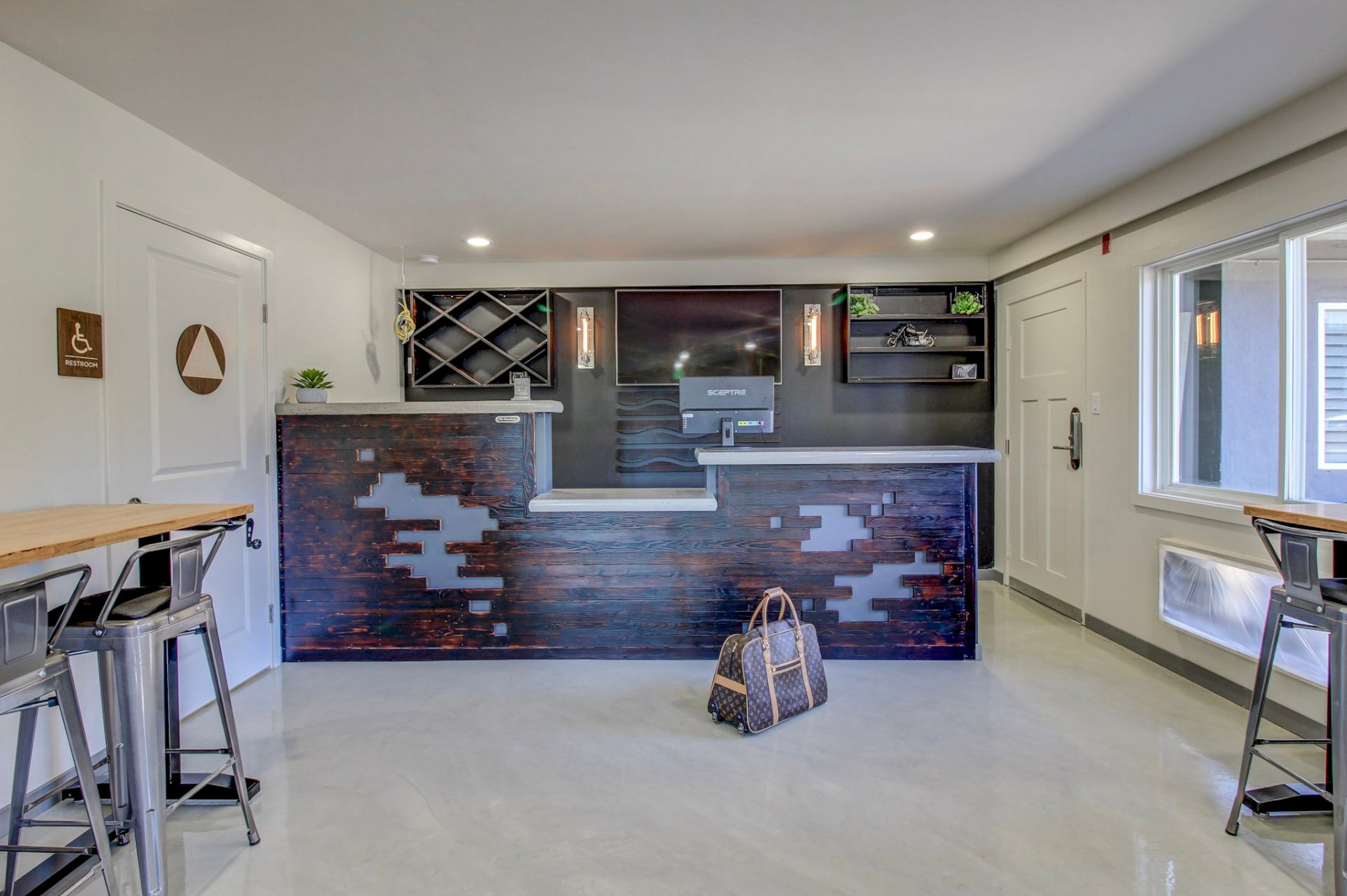 A modern bar area with a dark brick front, built-in shelves, a sink, and a small workflow. A bag sits on the floor, seating to the sides.