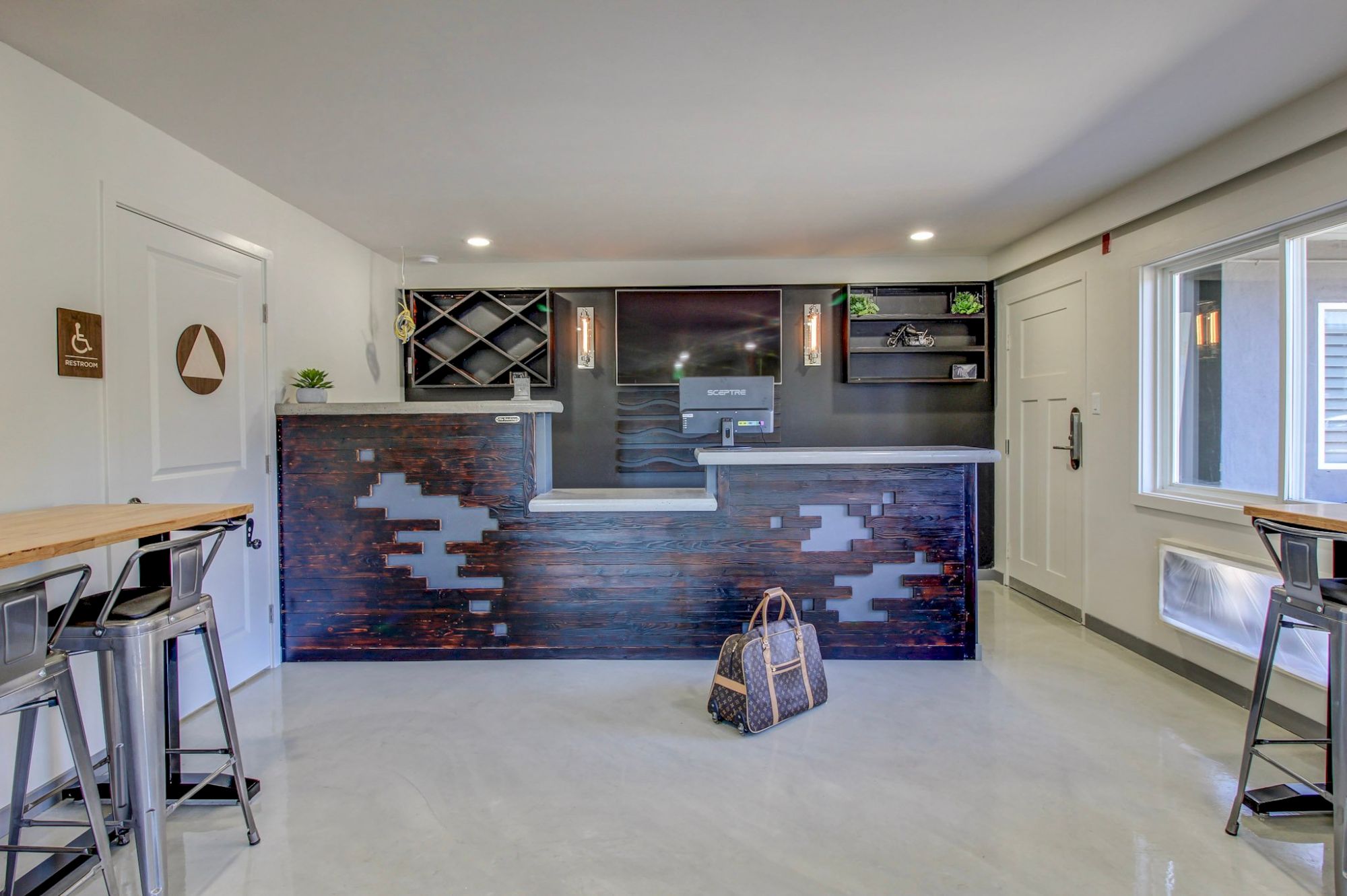 A modern bar area with a dark brick front, built-in shelves, a sink, and a small workflow. A bag sits on the floor, seating to the sides.
