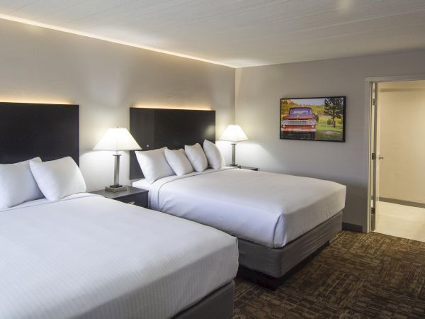 Two double beds with white linens and pillows, two bedside lamps, a dresser, and a flat-screen TV in a hotel room.