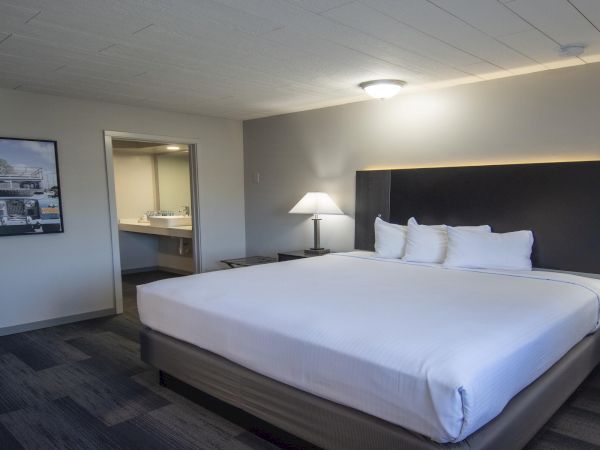 A clean hotel room with a large bed, nightstands, lamps, a desk and chair, and a doorway to a bathroom in the background.