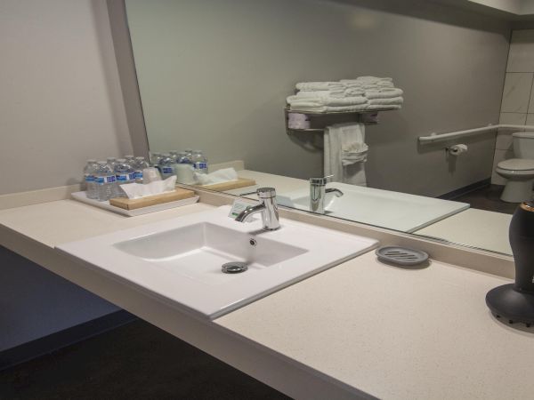 A clean hotel bathroom sink area with a double basin, mirror, stacked towels, bottled water, and a coffee setup on the counter ending this sentence.
