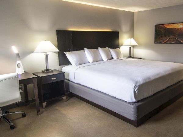 A tidy hotel room with a large bed, two nightstands, lamps, a desk and chair, and a framed picture on the wall.