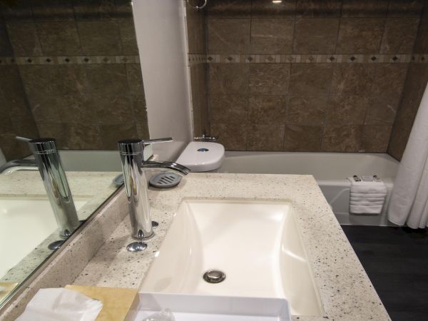 A modern bathroom vanity with two sinks, chrome faucets, a large mirror, and a bathtub/shower combo with white curtains and neutral tones.