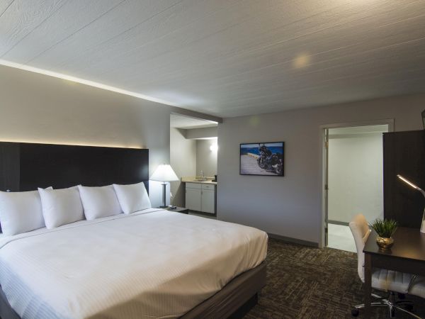 A modern hotel room with a large white bed, crisp linens, plush pillows, a nightstand lamp, desk area, and a doorway to a bathroom, airy vibe.