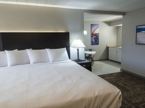 A modern hotel room with a large bed, bedside lamps, a desk and chair, and wall photos of a motorcycle ending.