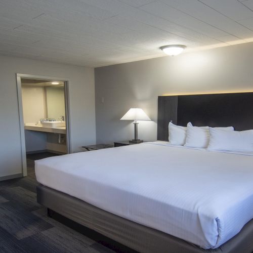 A bright hotel room with a neatly made king bed, bedside tables, lamps, and framed art on the walls.
