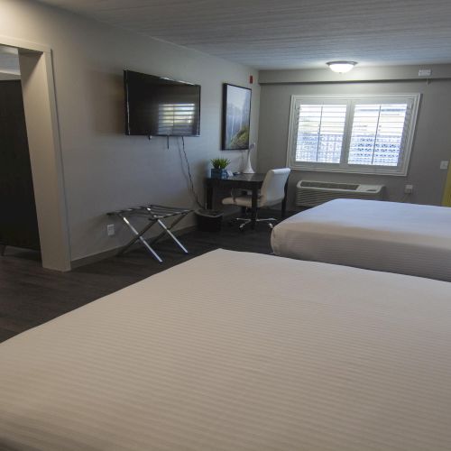 A modern hotel room with two beds, a wall TV, desk area, microwave, and a window with blinds.