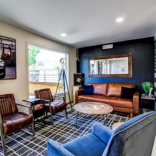 A modern lounge with leather and blue sofas, a round coffee table, a black accent wall, framed art, and a tall red-white flag mural.
