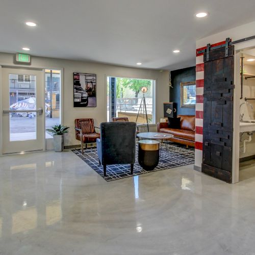 A modern lobby/lounge with exit sign, glass doors/windows, leather seating, and a small kitchenette/bar with sink and pipes.
