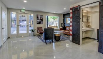 A modern indoor room lobby with chairs, a small table, and a bar display area with a sink and pipes.
