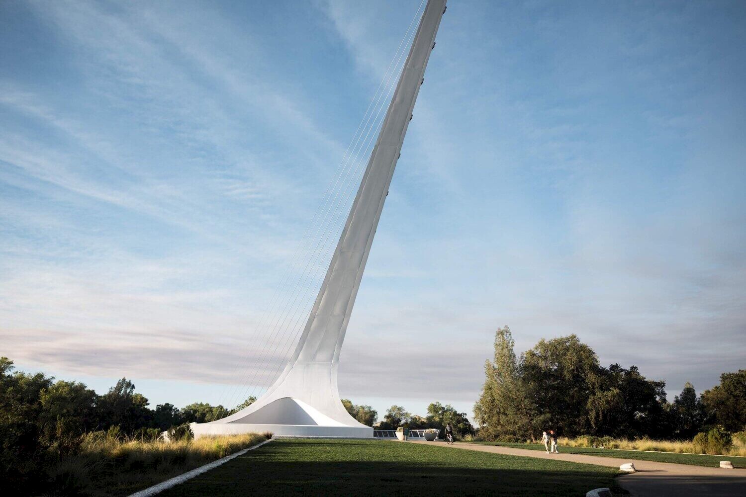 A dramatic cable-supported tower rises from a landscaped park, with lawns and a large white pavilion beneath it.