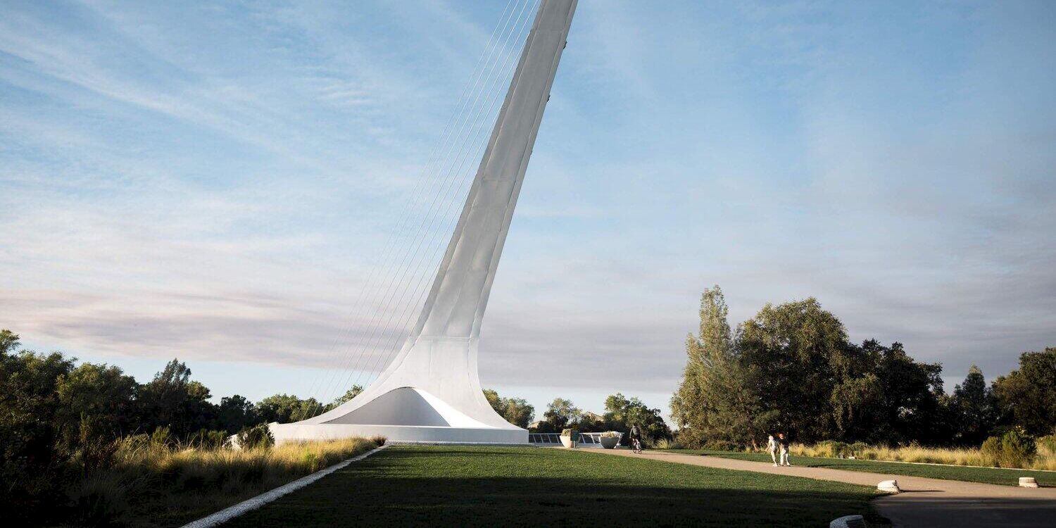 A dramatic cable-supported tower rises from a landscaped park, with lawns and a large white pavilion beneath it.