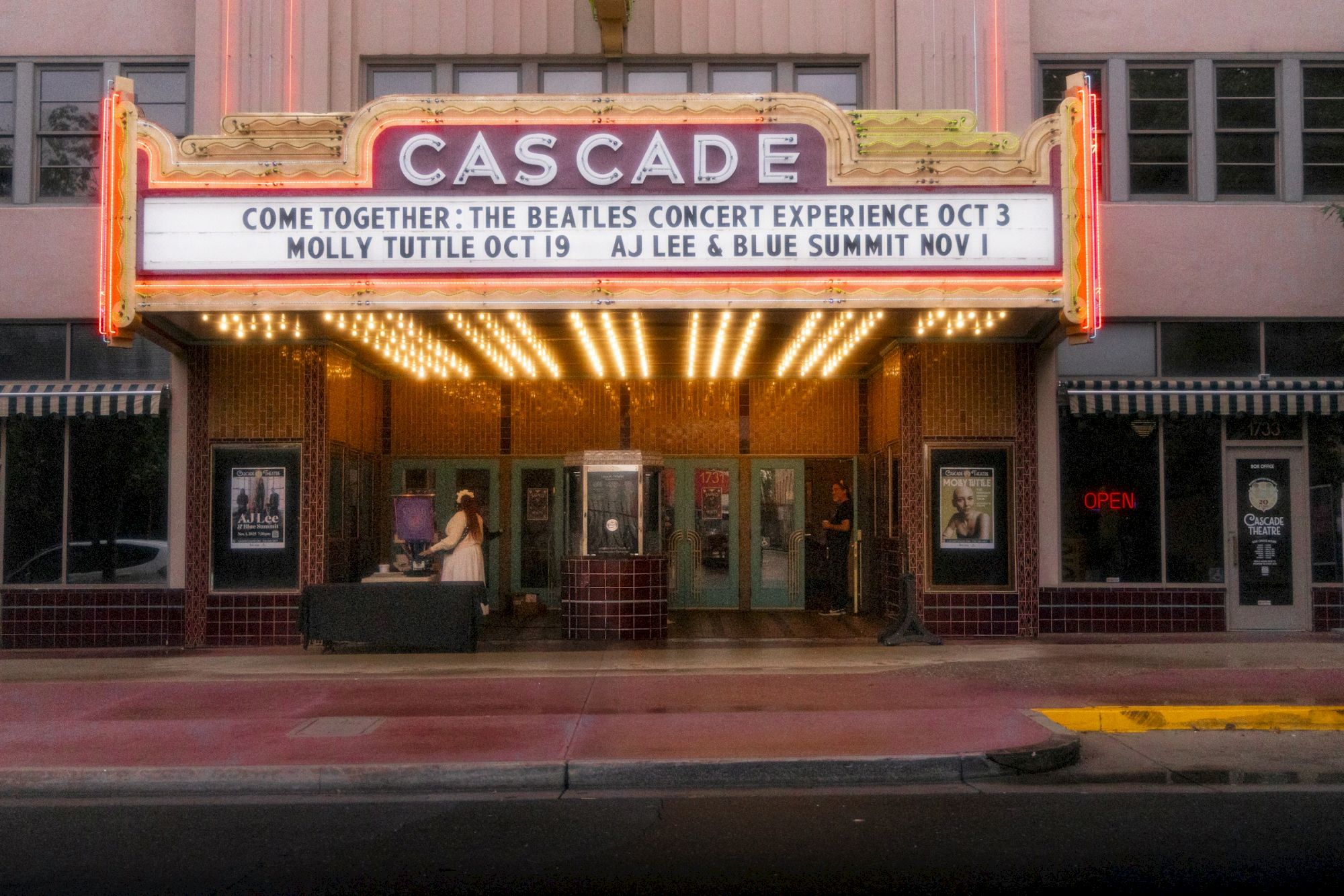 A lit Cascade Theatre marquee advertises a Beatles-themed concert experience, listing &ldquo;Come Together&rdquo; and performers with dates.