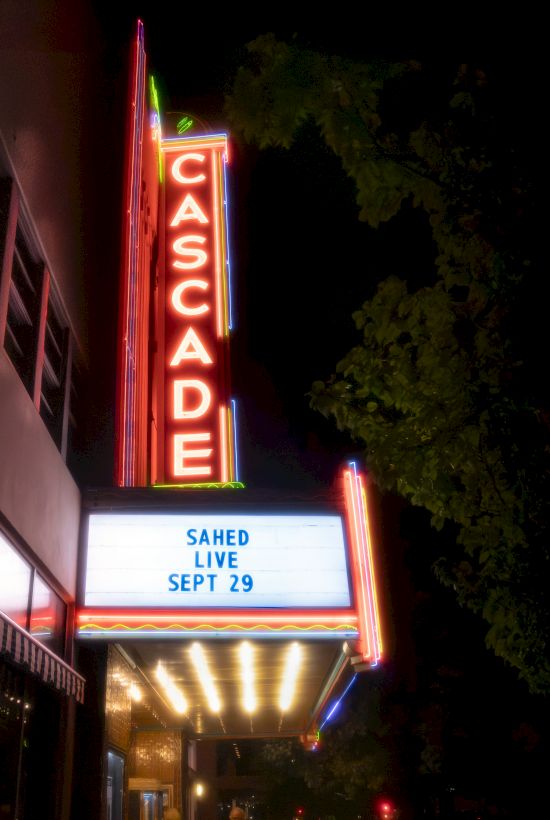 Neon marquee reads &ldquo;CASCADE&rdquo; and &ldquo;SAHED LIVE SEPT 29&rdquo; on a night street with trees behind it.