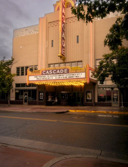 A Cascade Theatre marquee outside a building glows with ads for &ldquo;Come Together: The Beatles Concert Experience&rdquo; at dusk.