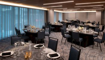 Elegant conference banquet hall with round tables set with glassware, cutlery, and candles under warm overhead lights.