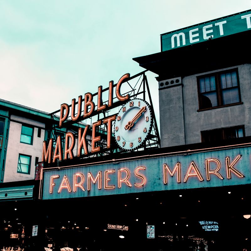 Photo shows the sign &ldquo;Dubuque Market Place&mdash;Farmers Market&rdquo; with a large clock on a building.
