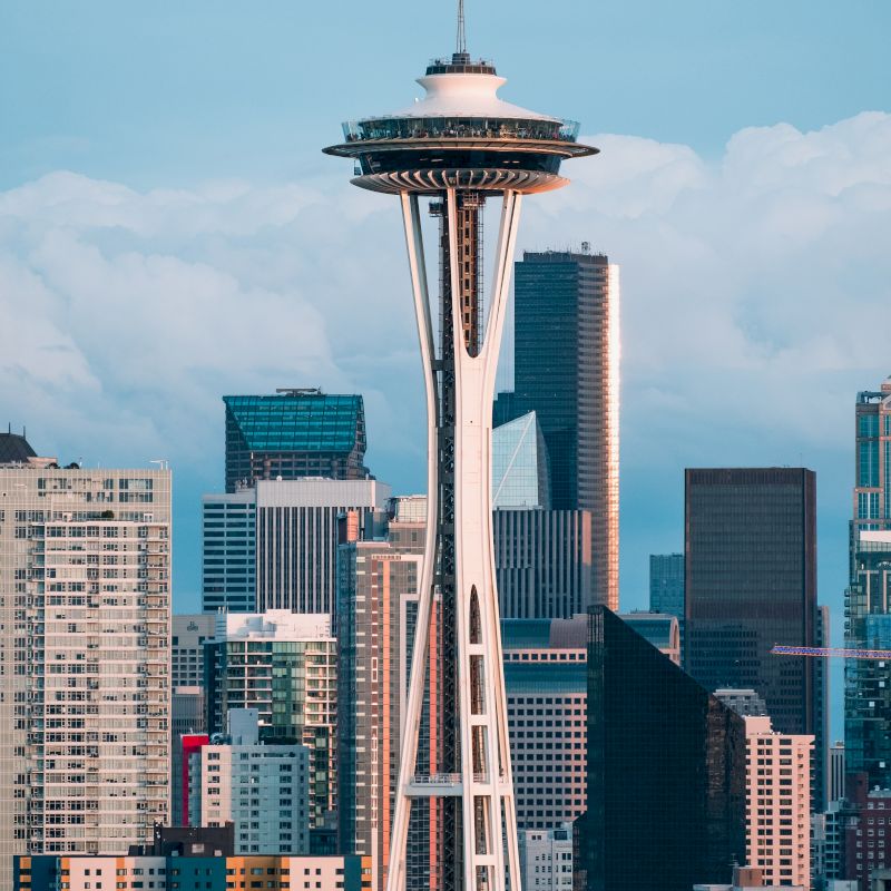 A city skyline with the Space Needle&rsquo;s observation deck rising above downtown under a blue sky.