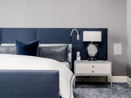 A modern hotel bedroom: bed with blue pillows, bedside lamp, TV remote, clock, and a geode-like decor on the nightstand.