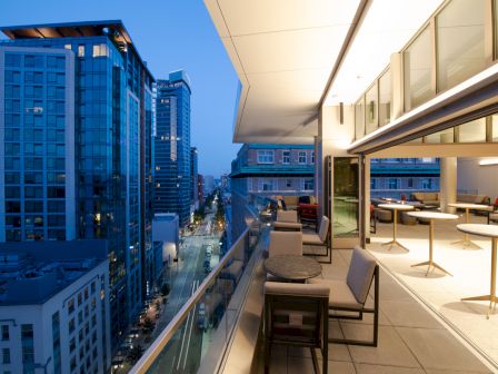 A high-rise city view from a modern apartment terrace with stylish outdoor seating and big glass windows, overlooking downtown streets.