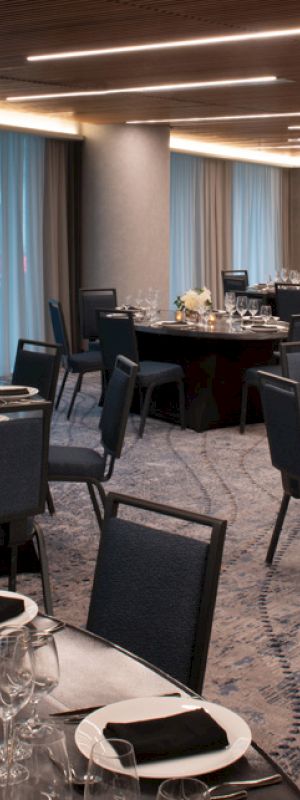 A modern event banquet setup with neatly set round tables, place settings, glassware, and candles in a conference-style room.