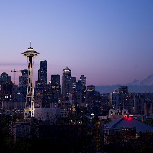 Seattle at dusk&mdash;skyline lights with the iconic Space Needle rising above the city and distant mountains.